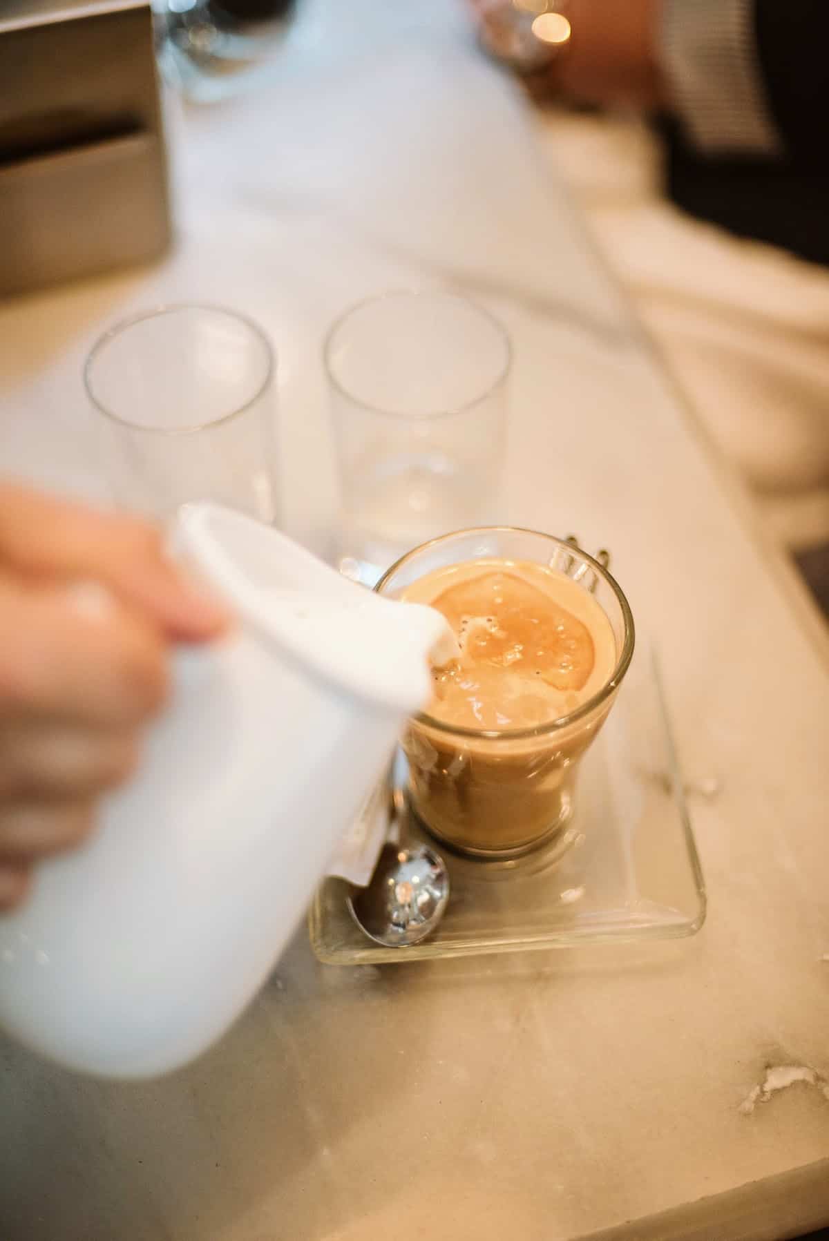 Overhead shot of a person pouring milk into a clear glass of coffee