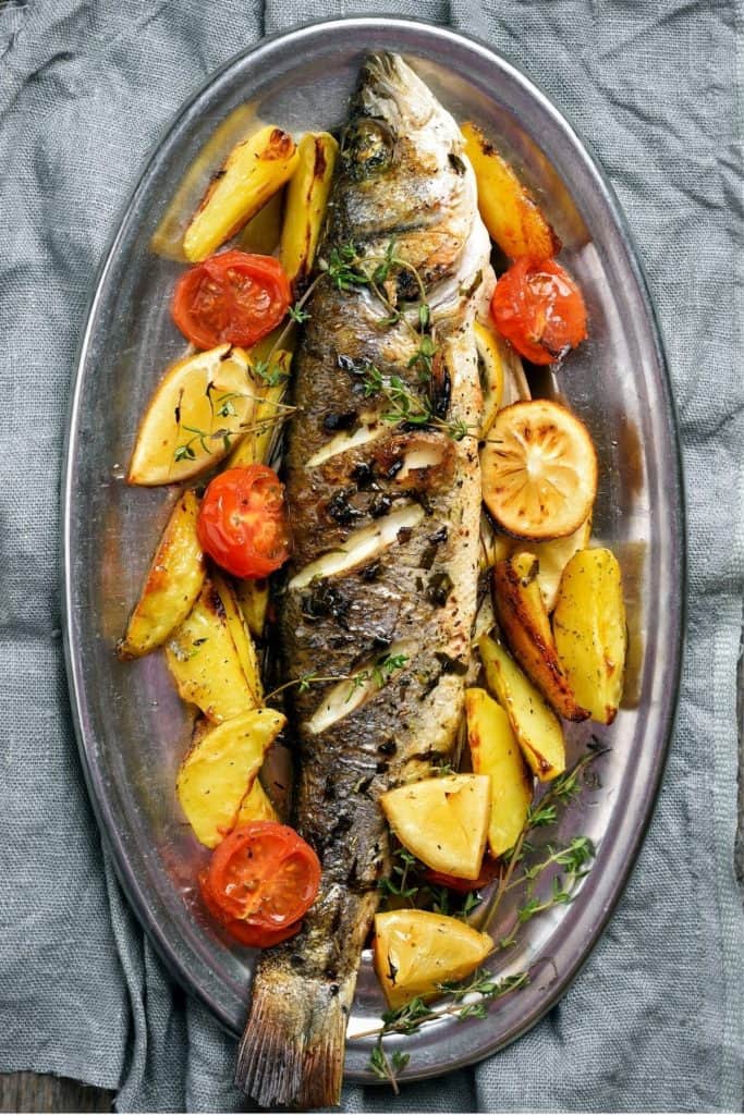 Roasted fish with lemon, tomato and potatoes on an aluminum platter