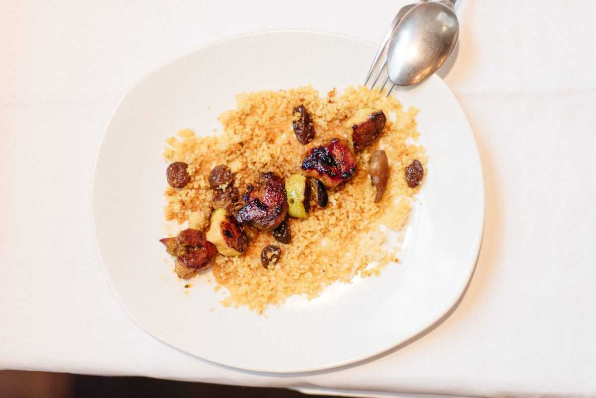 Grilled lamb with zucchini and dates served over cous cous on a white plate.