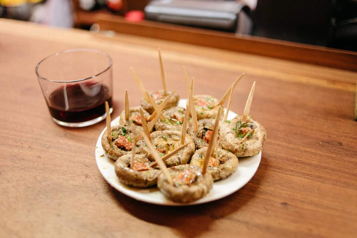 Chorizo-stuffed mushrooms on a white plate beside a short glass of red wine.