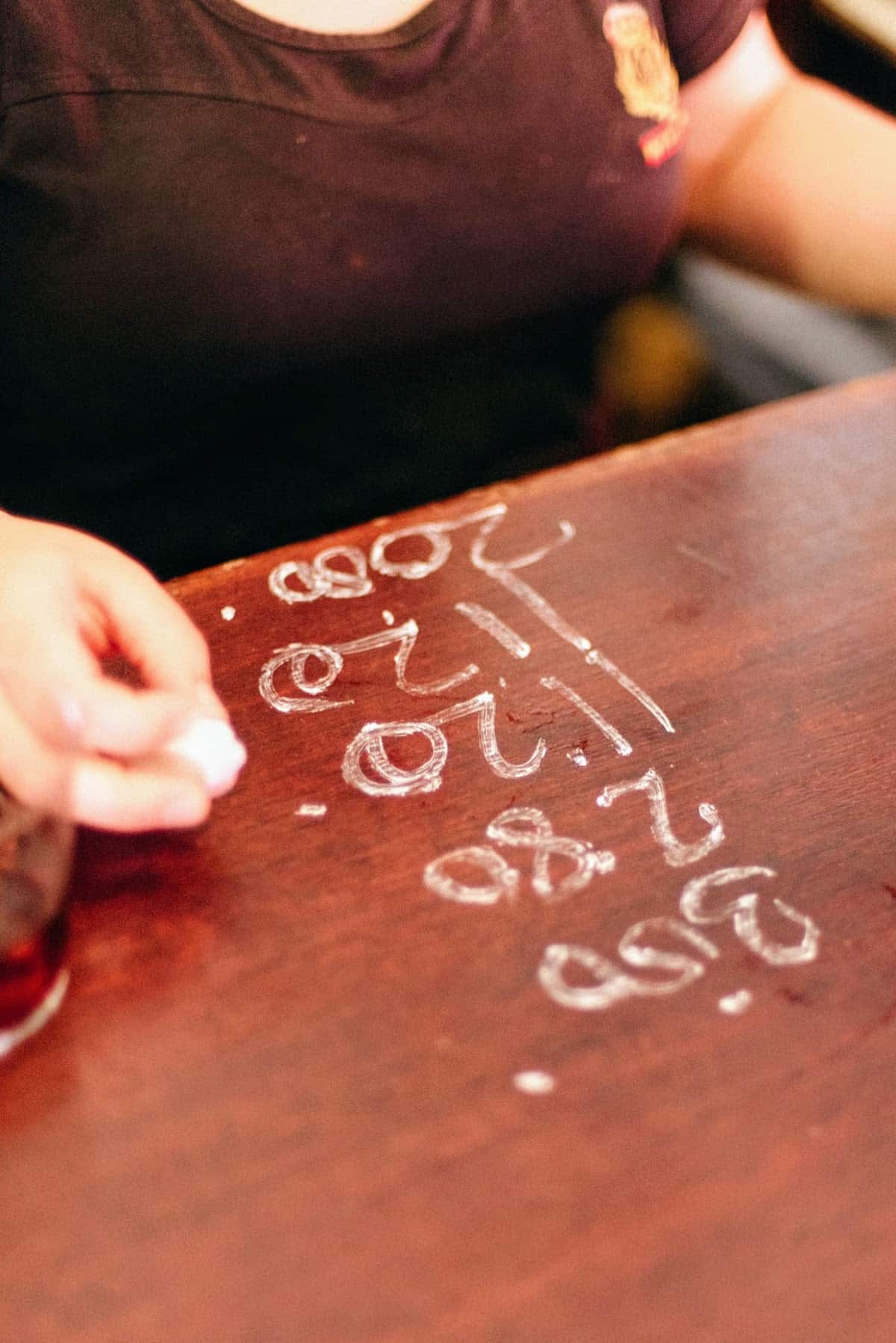 Close up of a bartender writing a client's tab in chalk on a wooden bartop