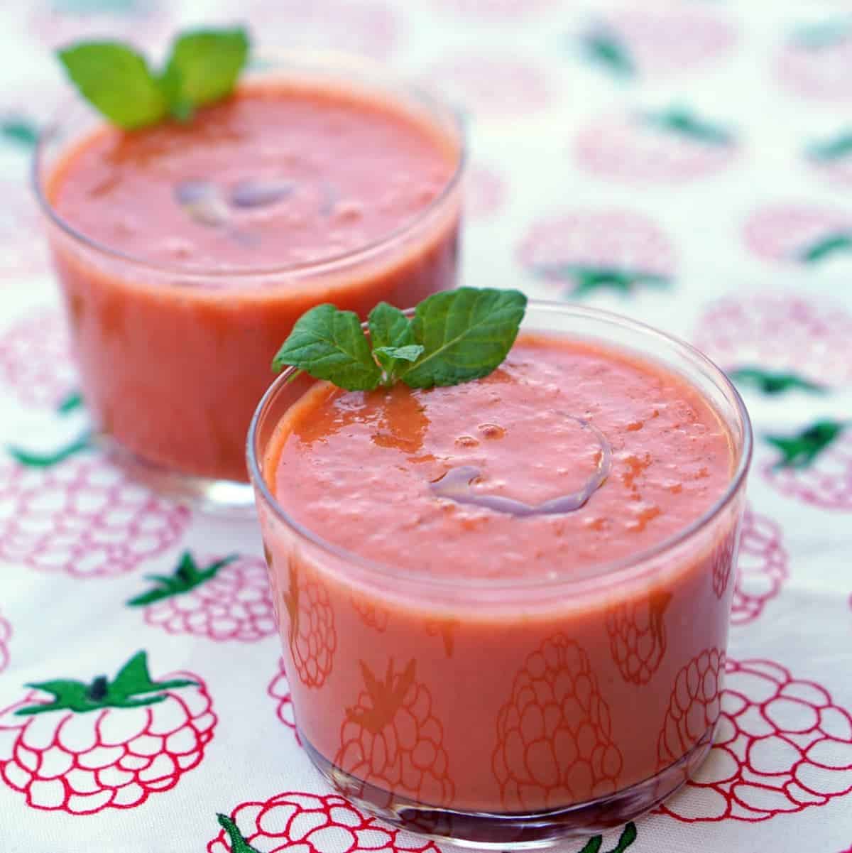 Two clear glasses of watermelon gazpacho garnished with mint.