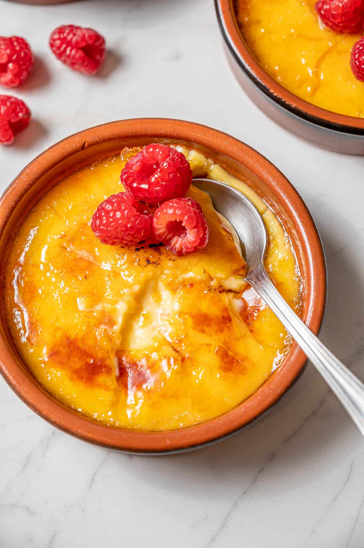 Crema Catalana (the Spanish creme brulee) in a clay dish with a few raspberries on top. A silver spoon cracked into the sugar crust.