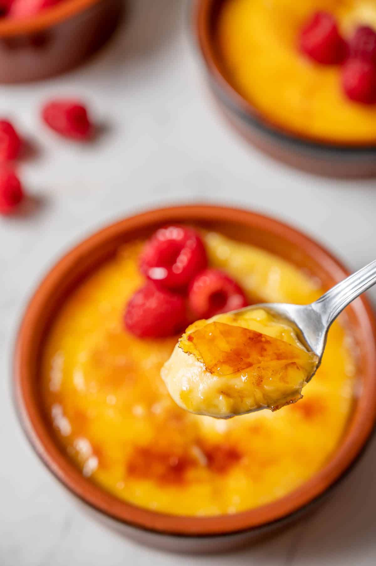Close up of a spoonful of crema Catalana with clay dishes of more crema catalana in the background.