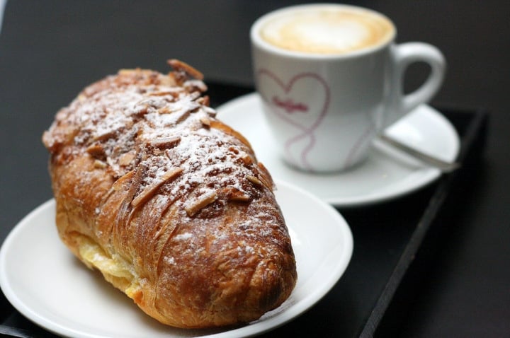 An almond croissant dusted with powdered sugar, with a latte in the background.