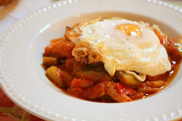 Bowl of Spanish pisto (tomato and vegetable stew) topped with a fried egg with crispy edges.