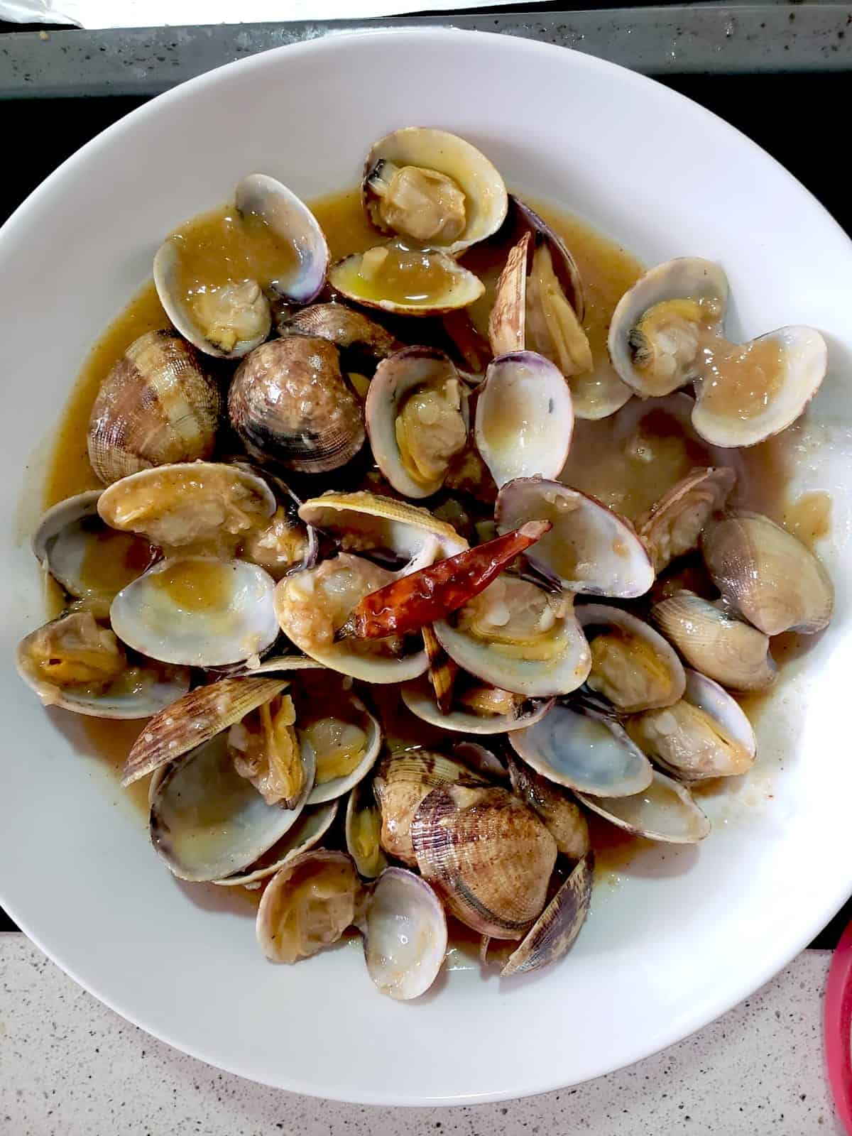 Overhead shot of small cooked clams in a white bowl