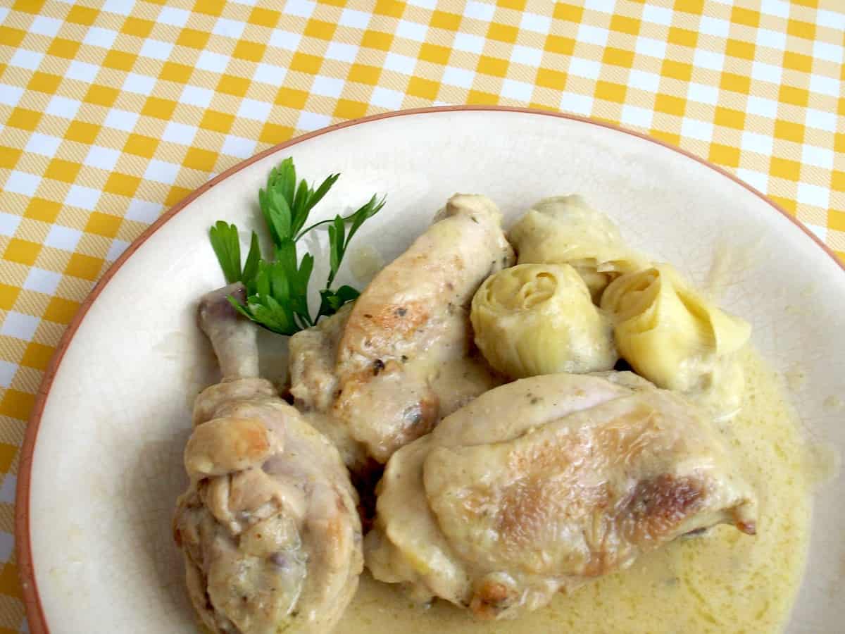 Chicken in a light colored sauce on a plate garnished with herbs
