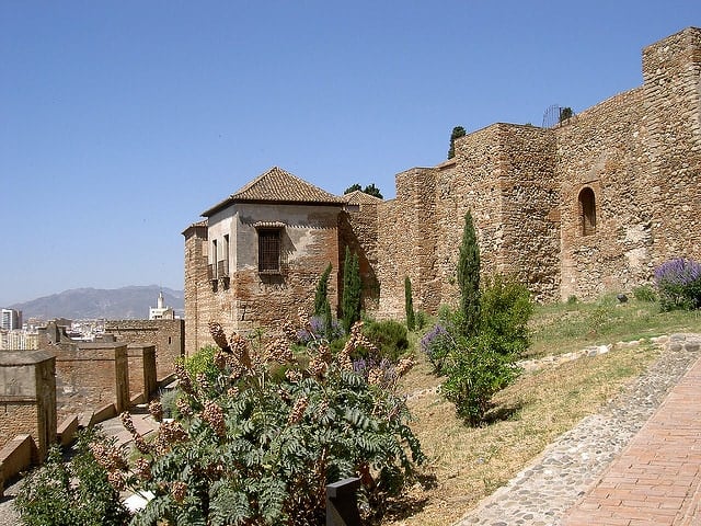 An ancient stone structure atop a hill with tall fortress walls and mountains in the distance.