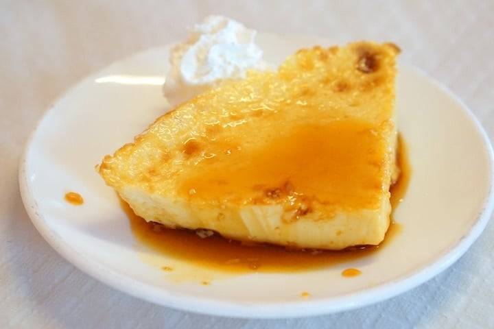 A slice of pale yellow Canarian flan with golden-brown caramel sauce and whipped cream.