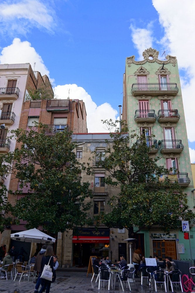 Colorful buildings with trees and people eating at cafe terraces in front of them.