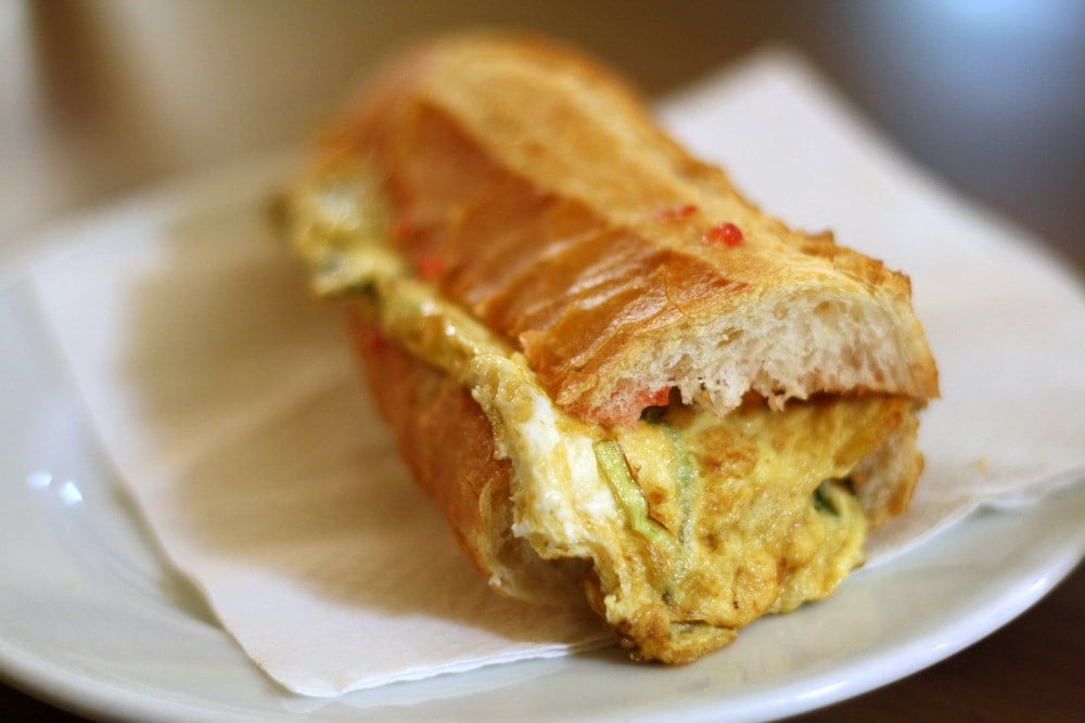 A crispy baguette sandwich with a thin omelette in the middle, on a white plate.