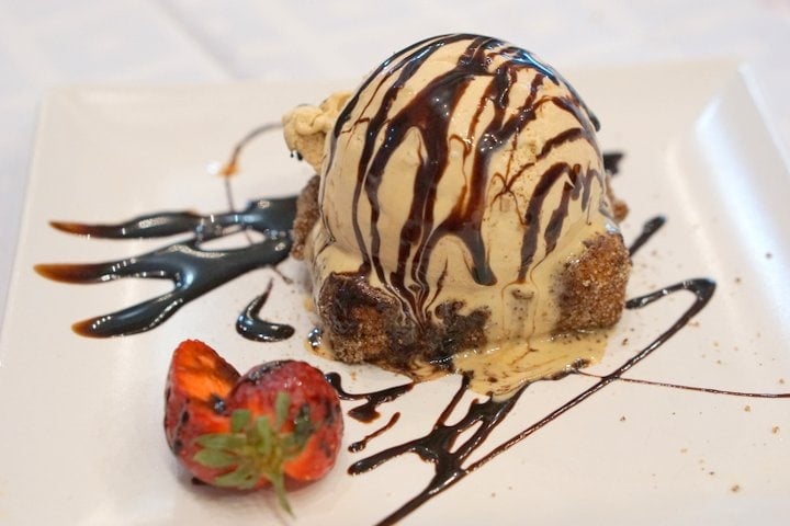 A scoop of beige ice cream drizzled with chocolate sauce atop a square of leche frita.