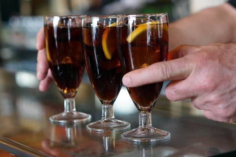 Gros plan d'un homme servant trois verres de vermouth avec des tranches d'orange.