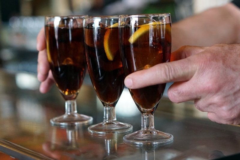 Close-up of a man serving three glasses of vermouth with orange slices.