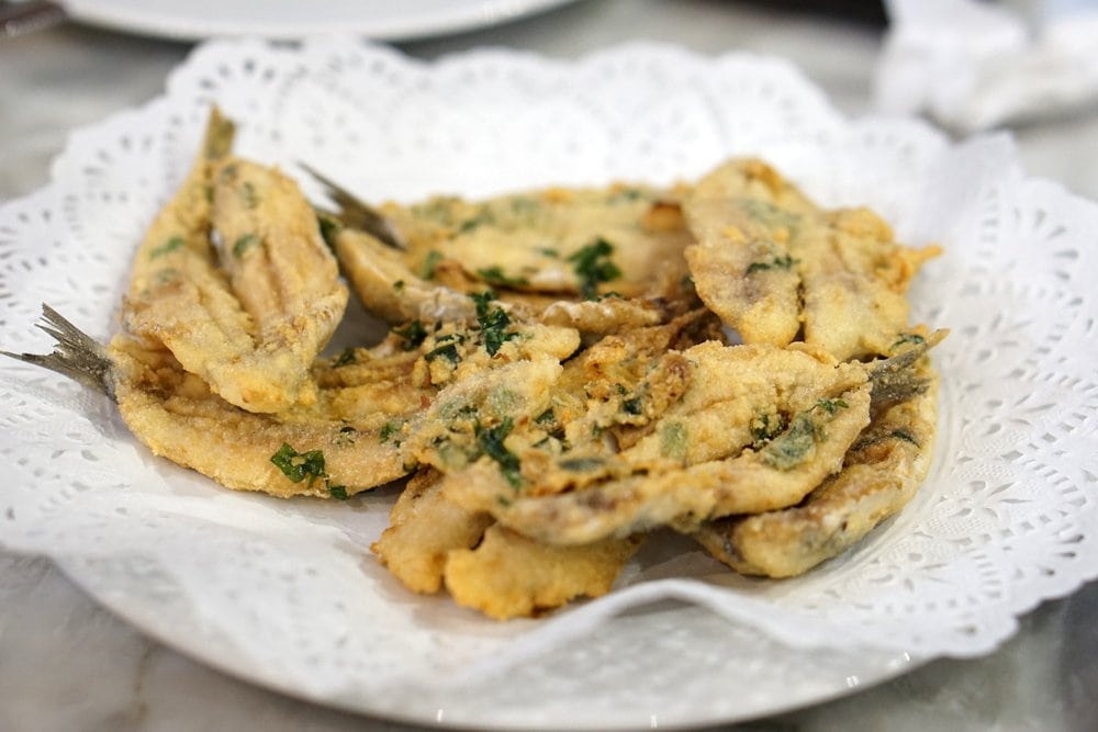 Deep-fried anchovies with herbs on a plate with a white doily.