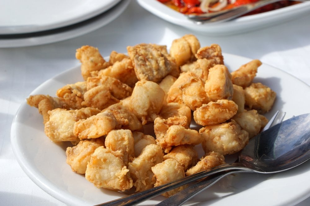 A plate of small pieces of deep-fried fish with two spoons beside it.