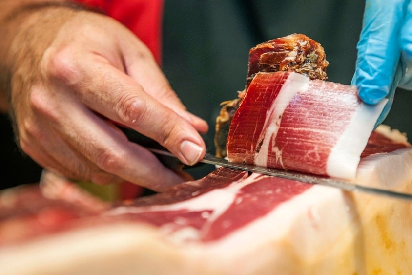 Close-up of a man shaving a thin slice off a leg of cured Spanish ham.