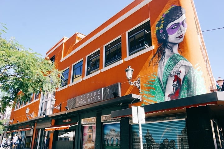 The bright orange facade of Antón Martín Market, with a colorful mural of a woman.