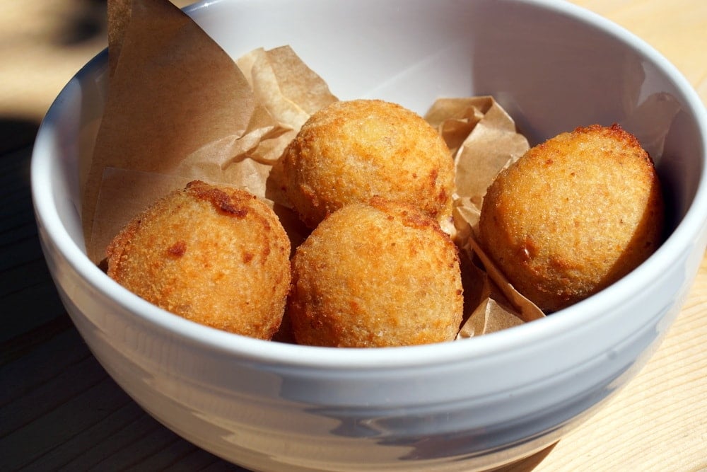 A bowl of four round deep-fried croquettes on a piece of brown paper.