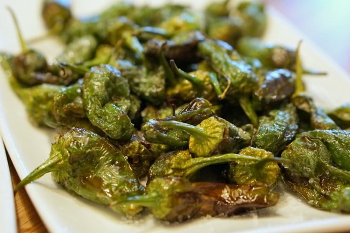 Close-up of small wrinkly green peppers, fried in olive oil and covered in flaky salt.