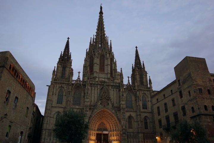 The Barcelona cathedral, an ornate Gothic building, at dusk.