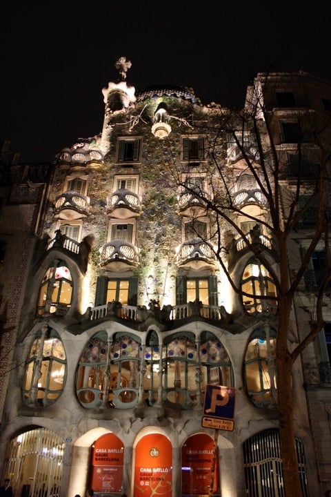 The undulating surrealist facade of a building by Gaudí, lit up at night.