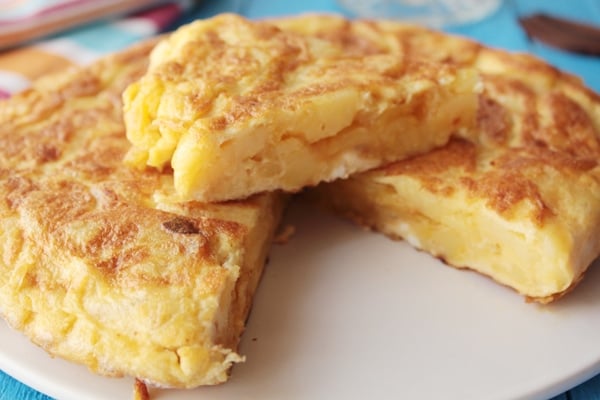 Close-up of a Spanish potato omelet with a large slice cut out and sitting on top.