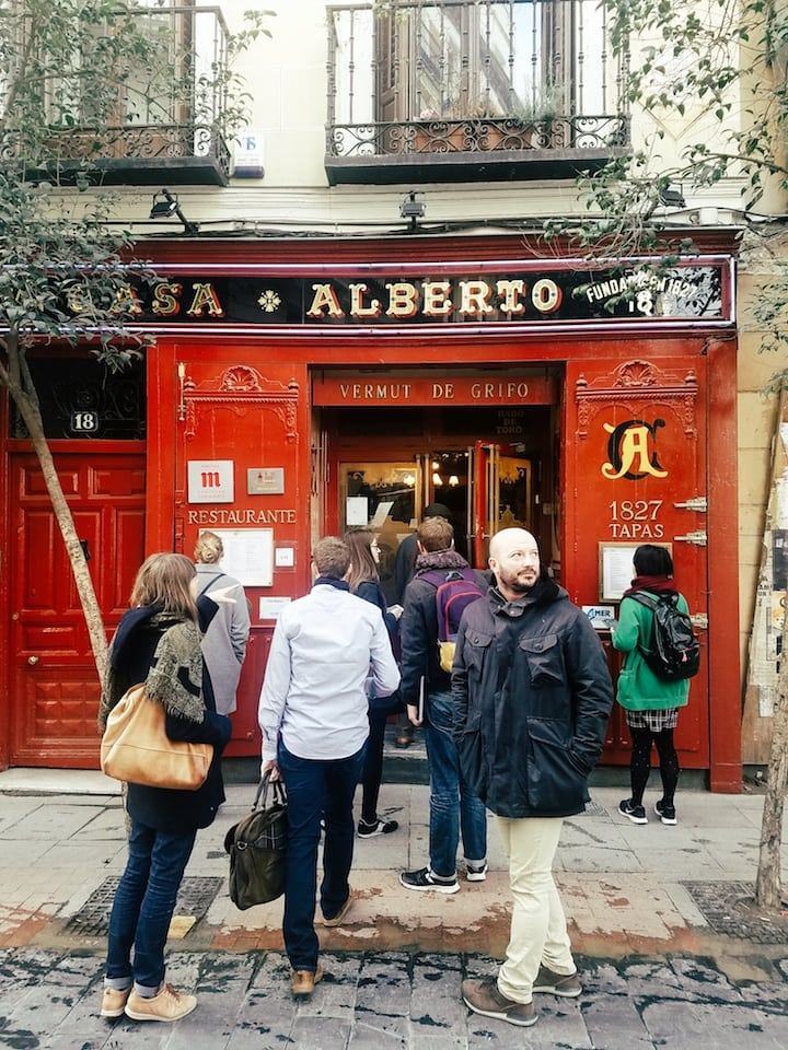 People standing in front of the red facade of Casa Alberto, a traditional bar in Madrid