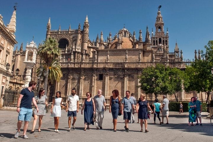 Several people walk toward the camera with Seville's cathedral in the background