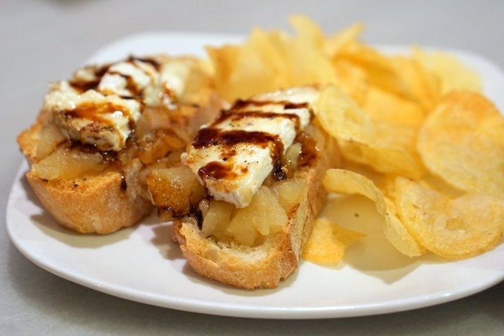 Small slices of bread topped with goat cheese and pear, with potato chips on the side