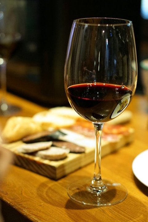 Close-up of a glass of red wine with a meat and cheese board in the background