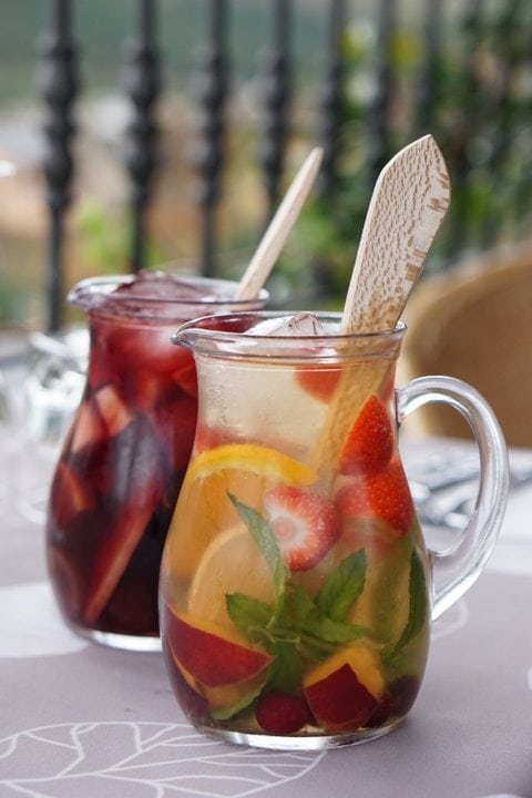 Two large pitchers of red and white sangria with fresh herbs and pieces of fruit.