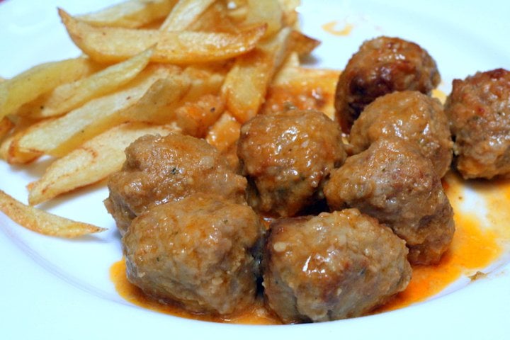 Close-up of meatballs in an orange sauce with fried potatoes on the side