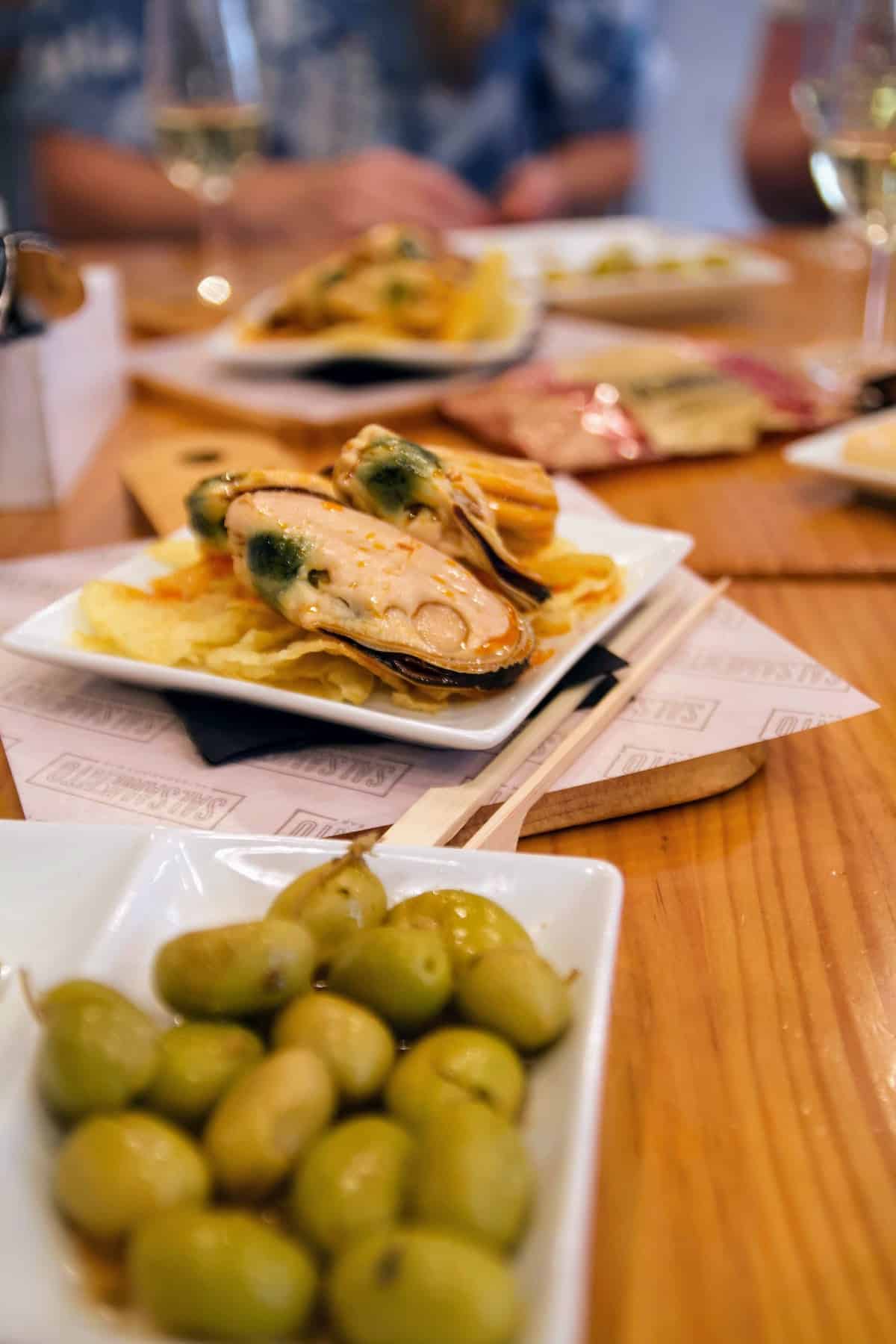 Mussels served over potato chips next to a dish of green olives