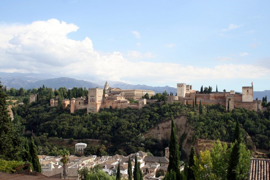 A wide view of the Alhambra, a large hilltop fortress surrounded by trees and mountains