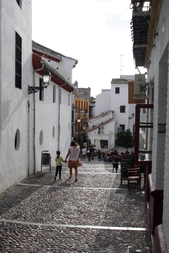 A woman and child walk down a cobblestone street between whitewashed buildings in the Albaicín