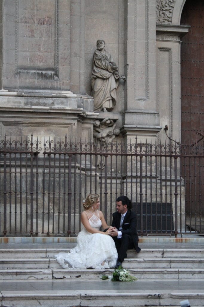 A bride and groom sitting on the stairs outside of the cathedral in Granada