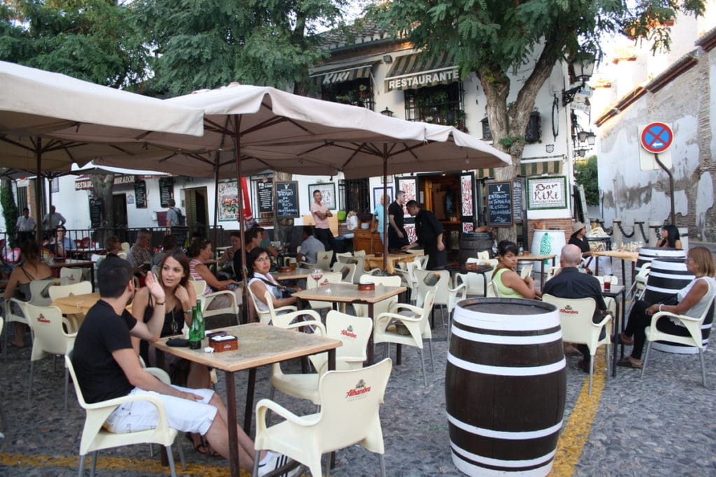 People sitting at tables under umbrellas in a traditional square in Granada