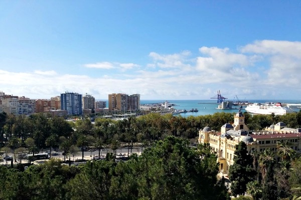 A panoramic view of an ornate old building, modern city, and the sea in the distance.