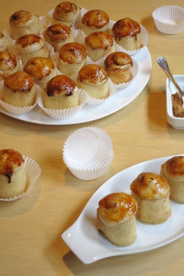 Several small cakes topped with golden-brown toasted cream, sitting in paper wrappers on white plates.