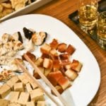 Different Turrón cut up on a white plate and served next to shot glasses of liquor.
