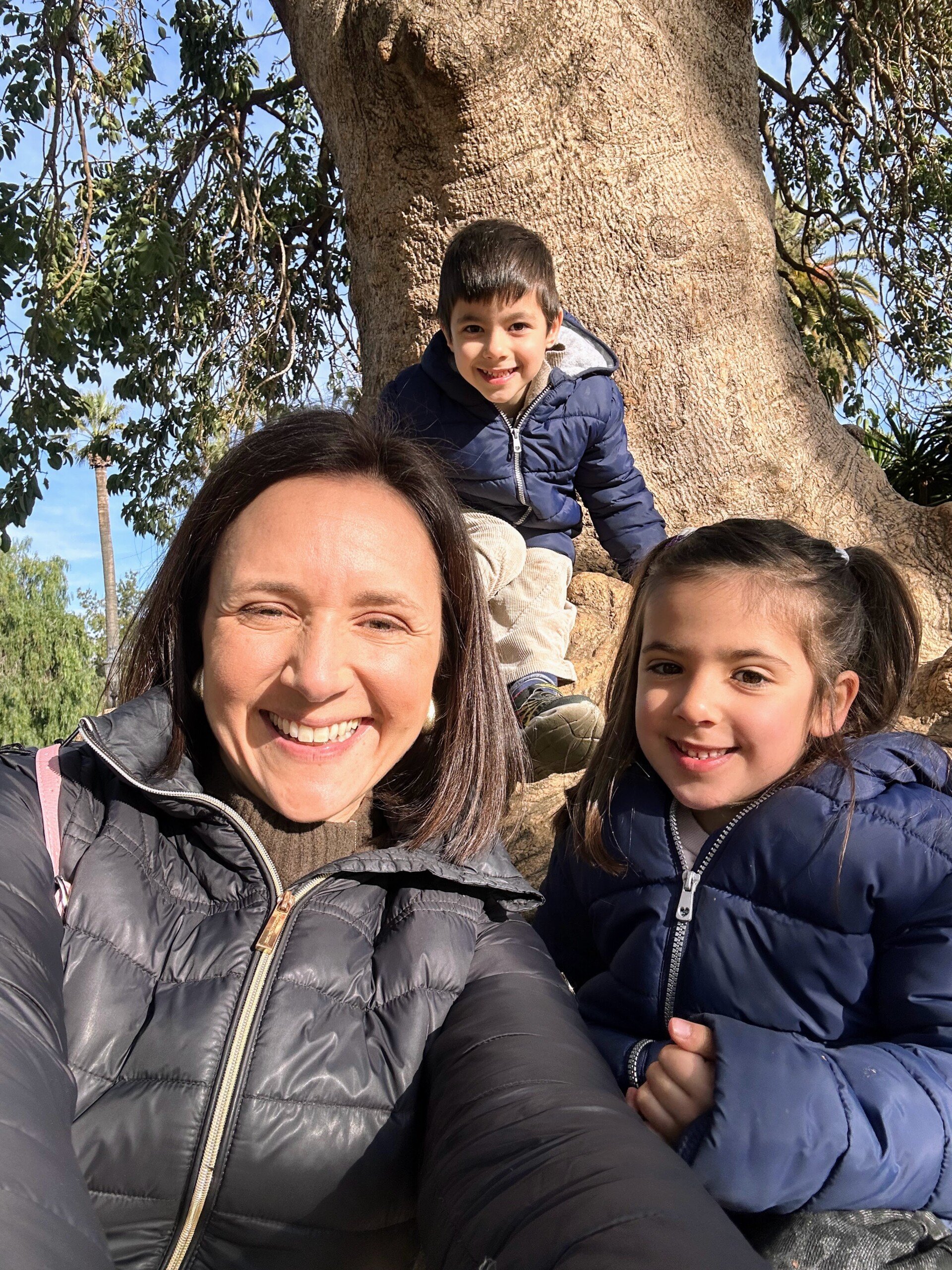 Mom with two kids in Barcelona sitting on a tree in the park.