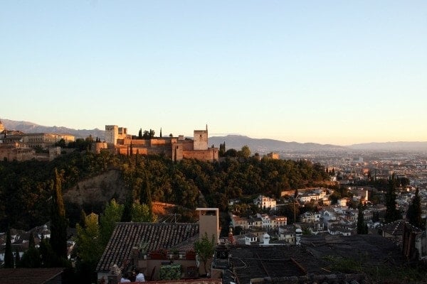 A panoramic view of Granada at sunset, with the Alhambra and mountains in the background.