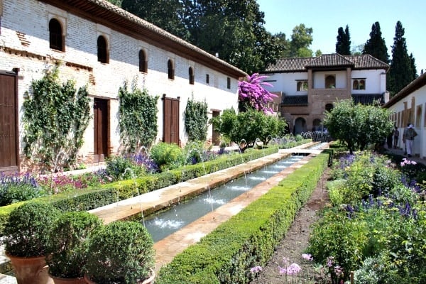 An inner courtyard of the Alhambra filled with green plants, hedges, and a long narrow fountain.