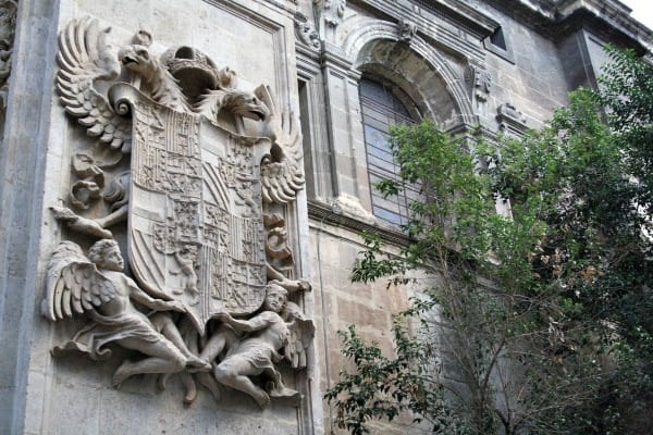 Close-up of an intricately carved stone coat of arms on the exterior wall of Granada's cathedral.