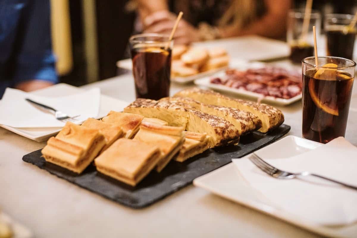 A tray with slices of baked empanada and Spanish omelet on a tabletop with Spanish vermouth.