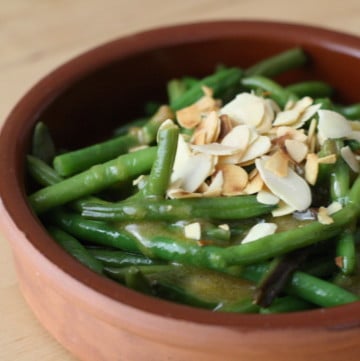 Green beans topped with slivered almonds in a small clay dish