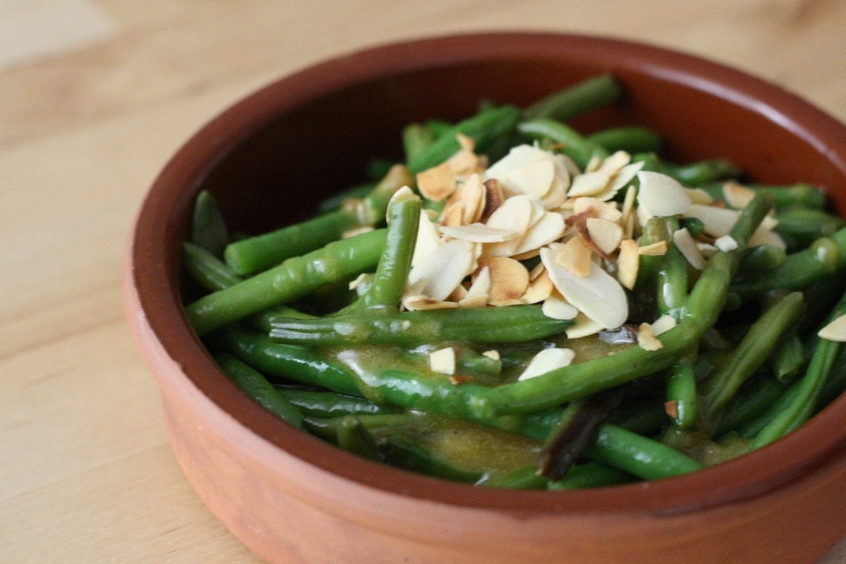 Green beans topped with slivered almonds in a small clay dish