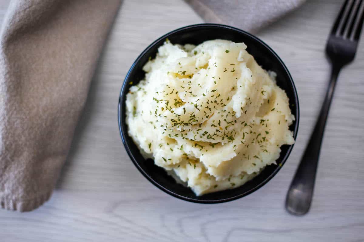 Bowl of mashed potatoes garnished with herbs on a tabletop